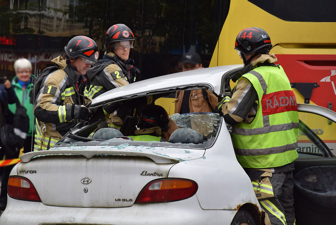 Tre brandmän lyfter ett uppklippt tak på en krockad bil.