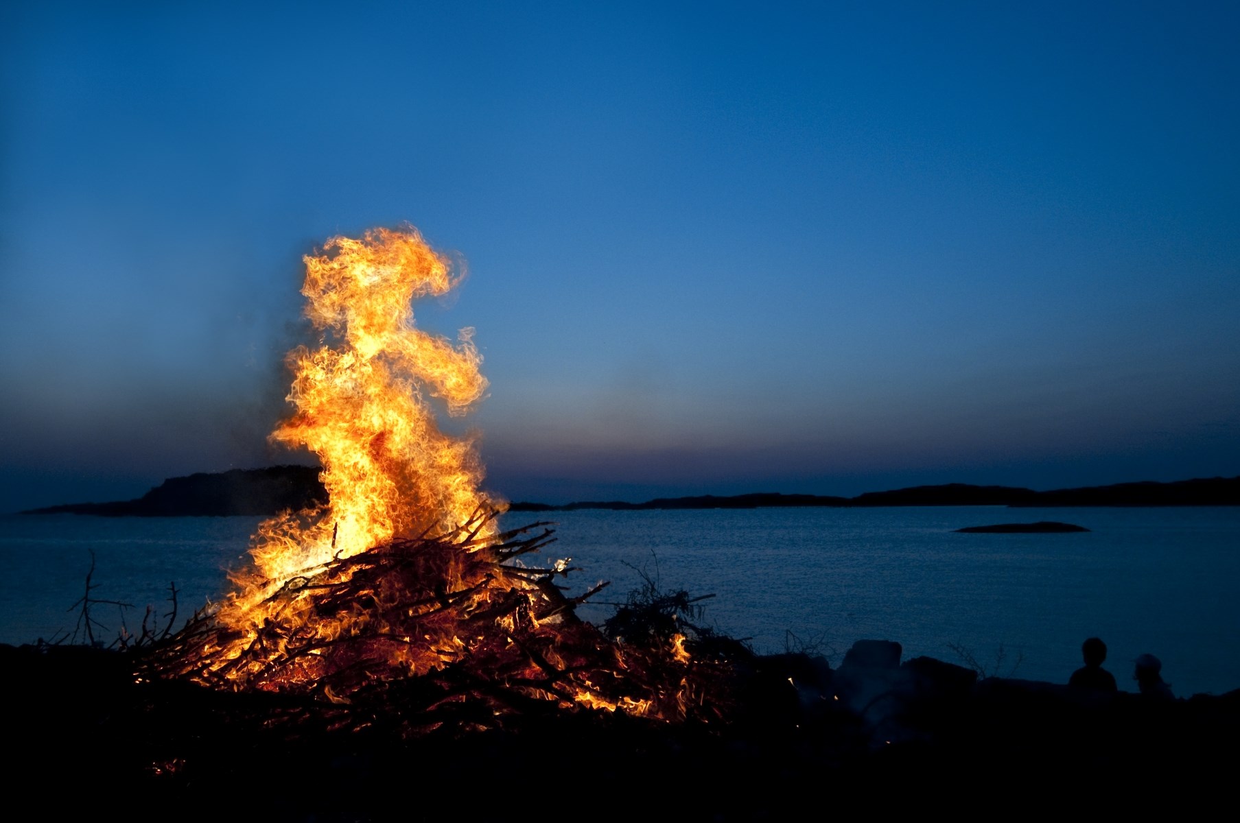 En brinnande Valborgsmässo eld syns utomhus i skymningen.